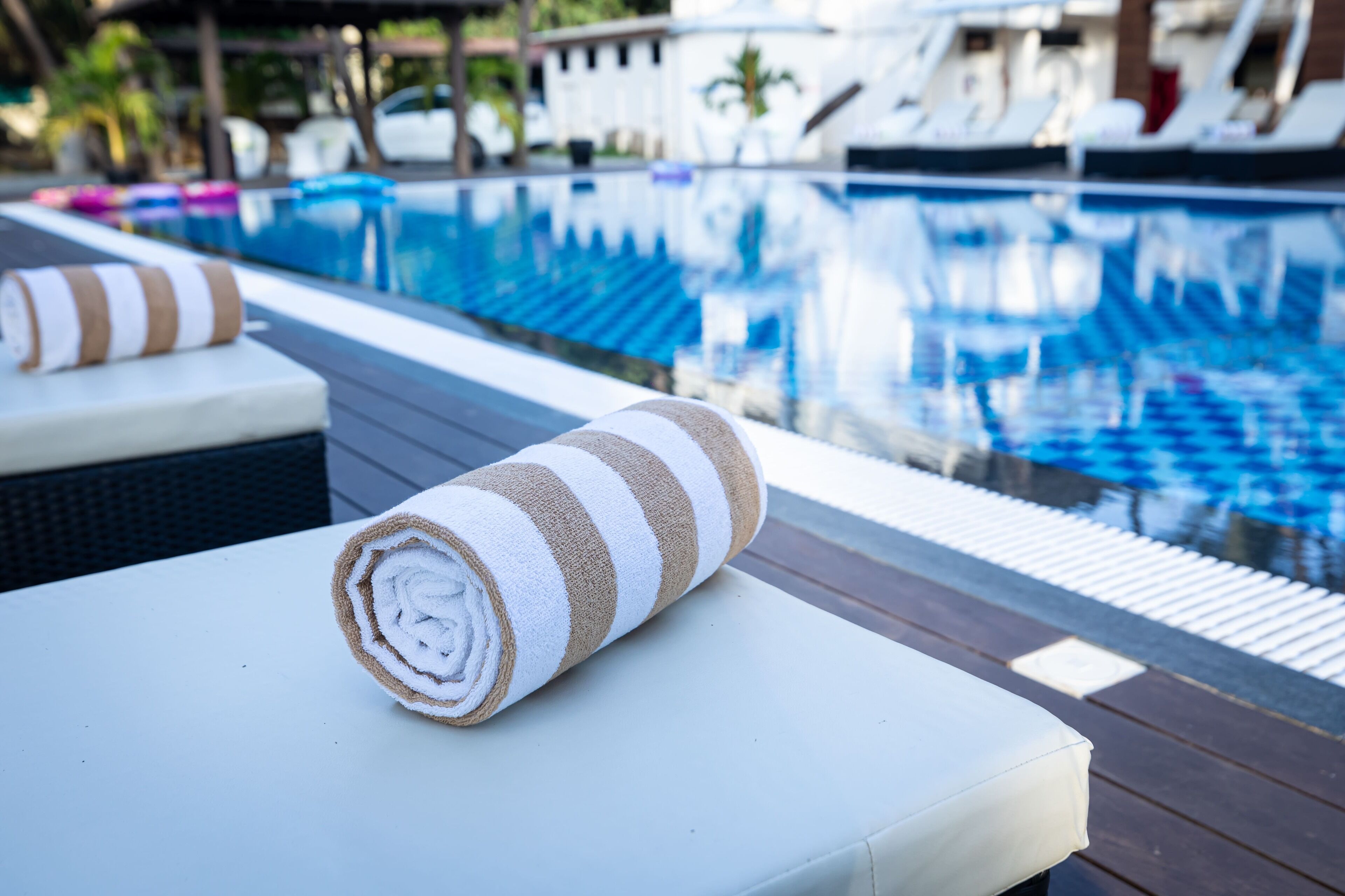A poolside area with a towel on a lounge chair, a pool with clear blue water, and lounge chairs in the background.