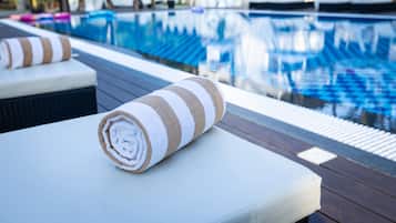 A poolside area with a towel on a lounge chair, a pool with clear blue water, and lounge chairs in the background.