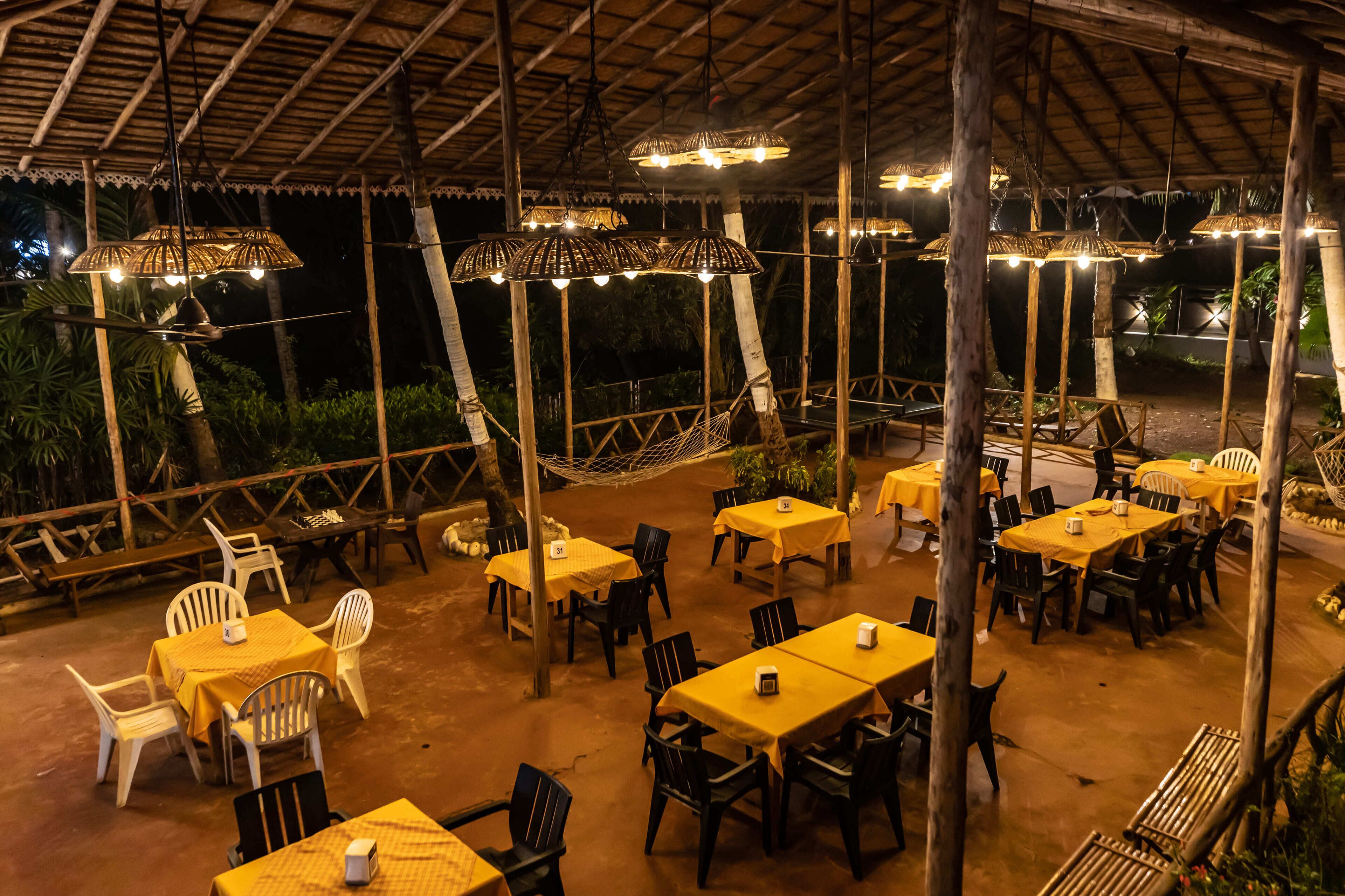An outdoor dining area with tables and chairs, covered by a roof with hanging lights.