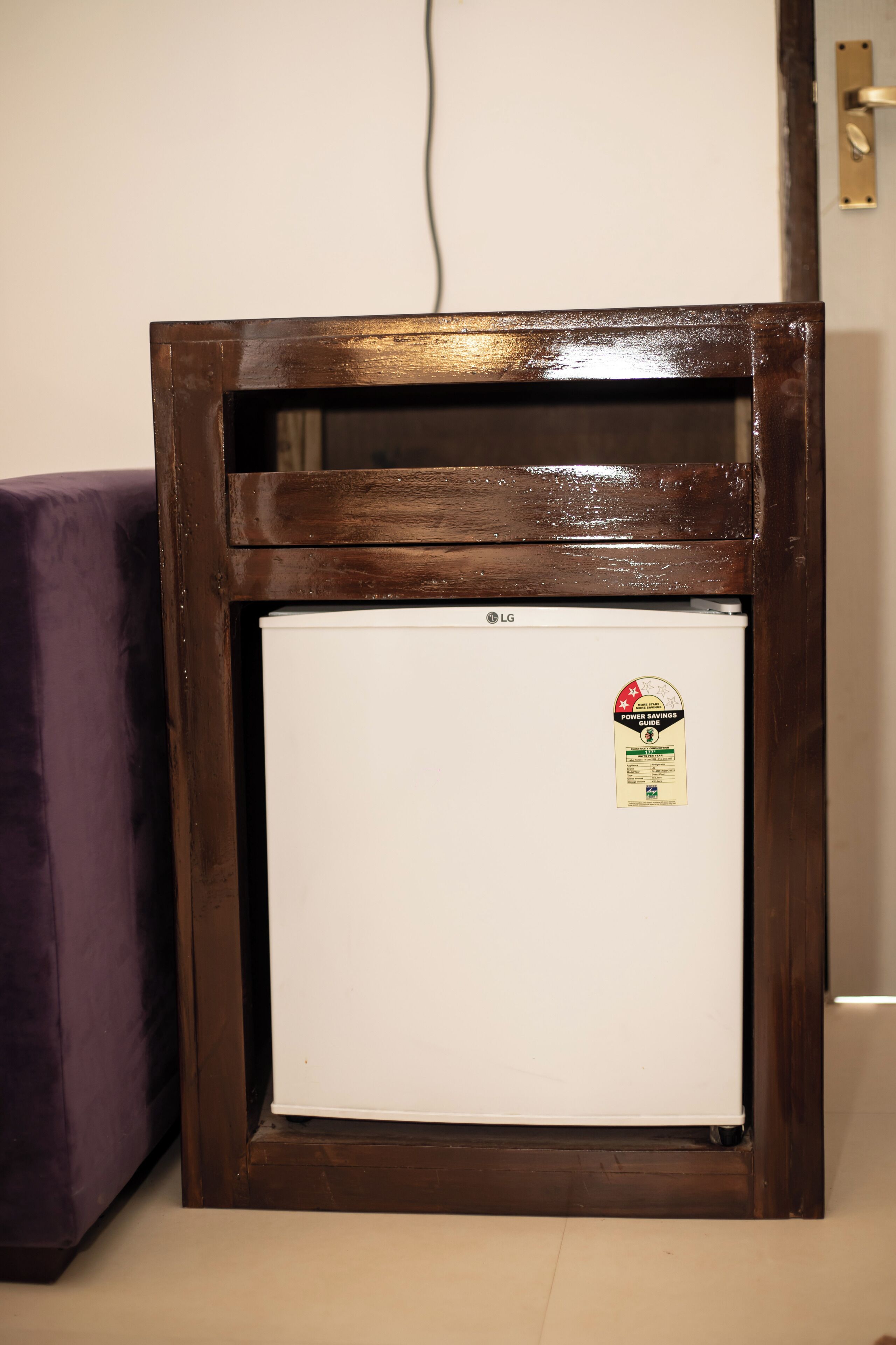 A white LG refrigerator with a sticker, placed in a wooden frame against a wall.