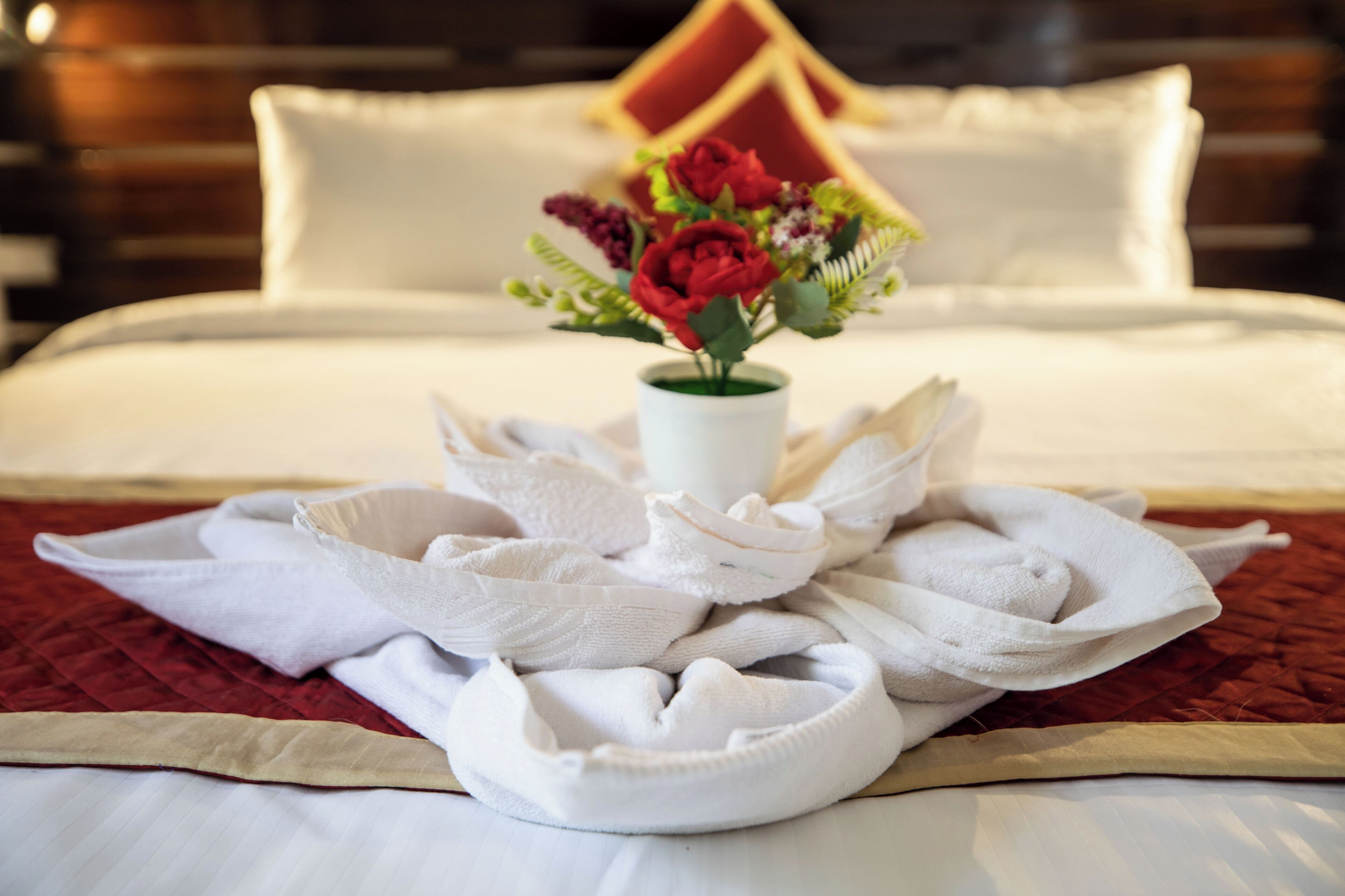 A neatly made bed with white linens, a bouquet of flowers in a vase, and a folded towel on the bed.
