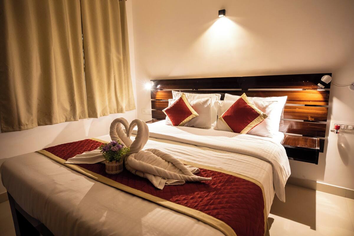 Una habitación de hotel con una cama bien tendida, un cabecero con estantes integrados y una mesita de noche con lámpara.