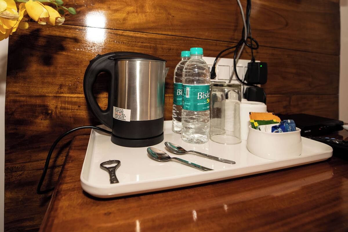 Una encimera de cocina con una tetera, botellas de agua Bisleri, un vaso, una taza blanca y una cuchara.