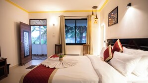 A hotel room with a large bed, a view of palm trees, and a door leading to a balcony. - The Woodside Inn Goa (Benaulim)