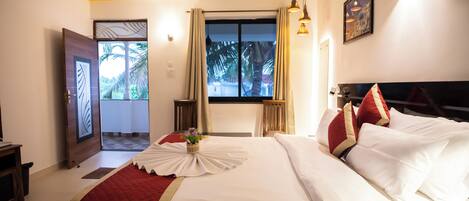 A hotel room with a large bed, a view of palm trees, and a door leading to a balcony.