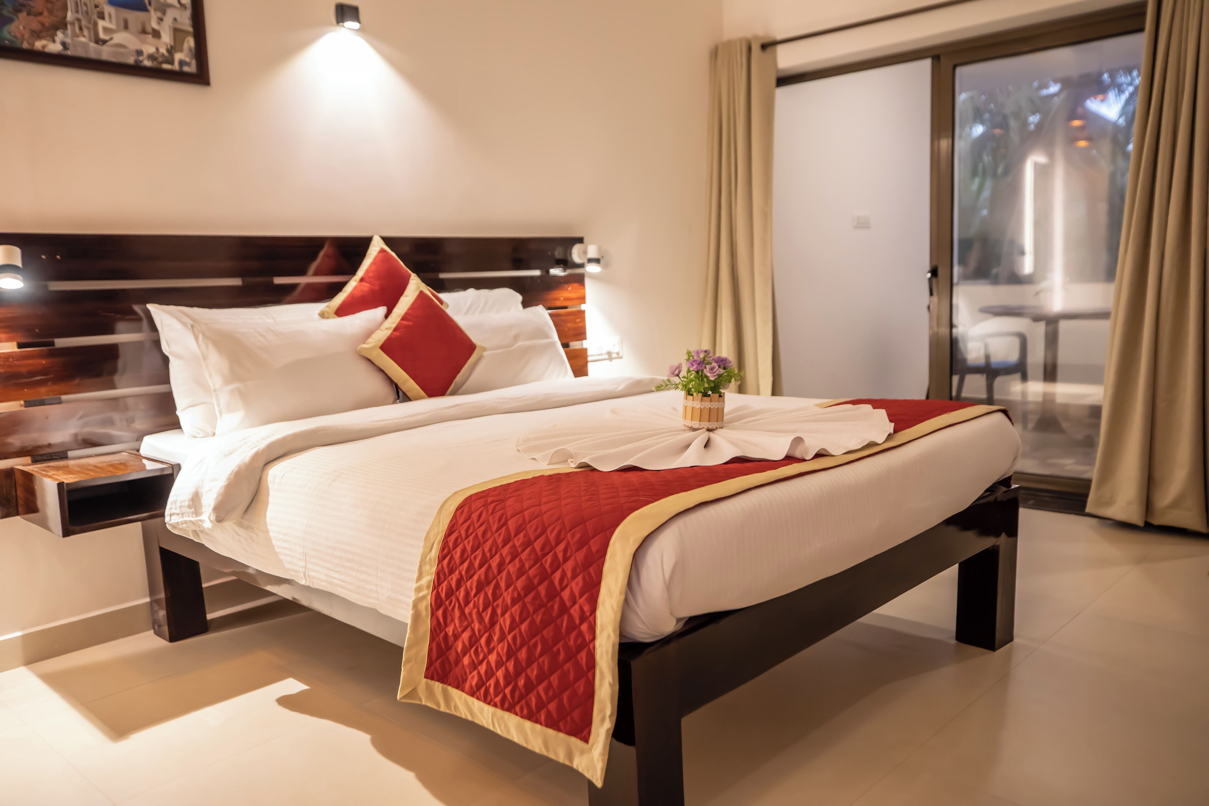 Una habitación de hotel con una cama grande, una mesita de noche, una pequeña mesa y vistas al exterior a través de una puerta corrediza de vidrio.