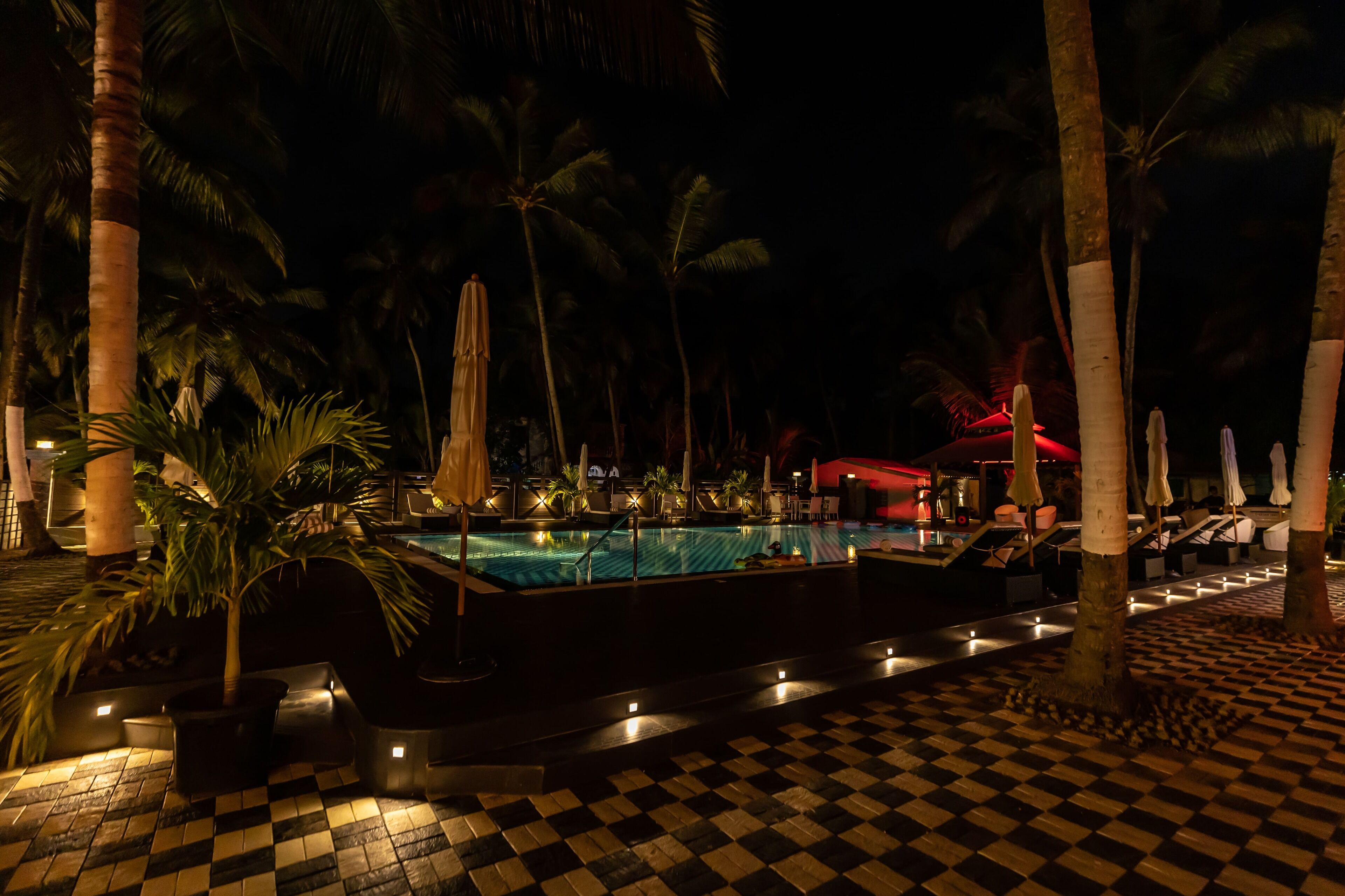 A nighttime pool area with a checkered floor, palm trees, and lounge chairs.