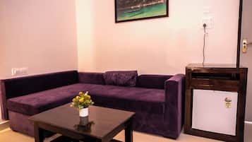 Una sala de estar con un sofá morado, una mesita con un florero y un mini refrigerador blanco.
