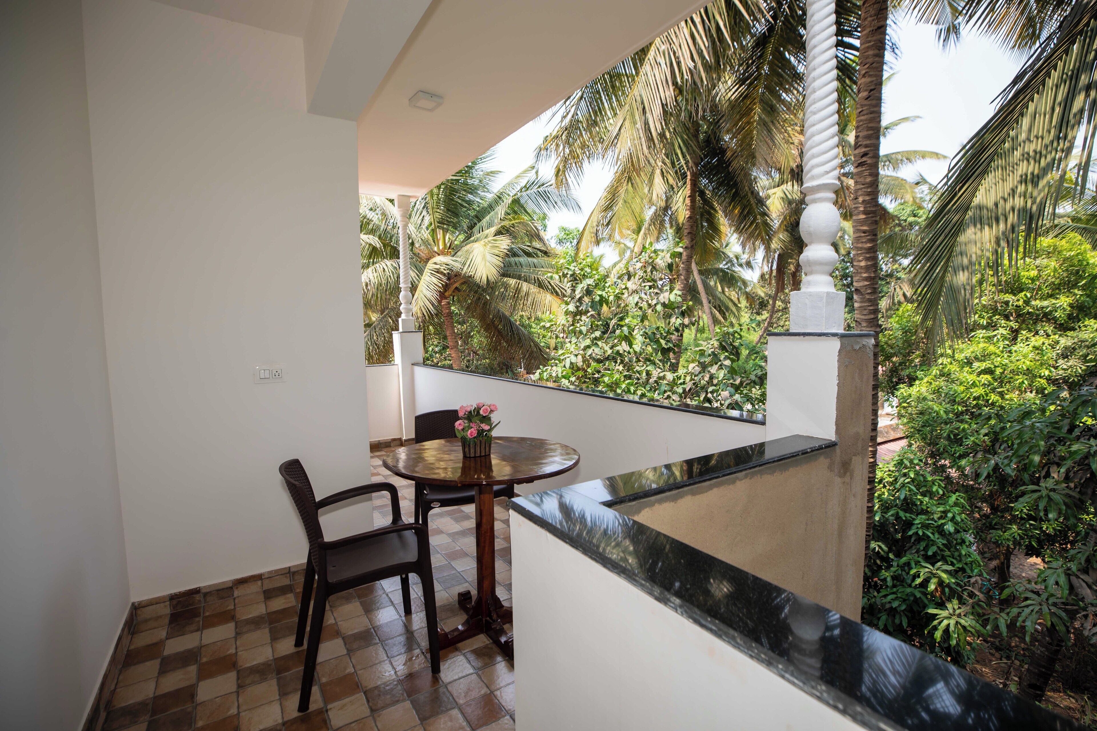 Un balcón con mesa y sillas, con vistas a un exuberante jardín de palmeras.