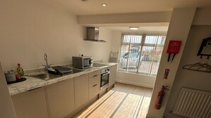 A modern kitchen with a built-in oven, a microwave, and a sink. There is a window with blinds, a fire extinguisher, and a radiator. - The Highmead (Blackwood)