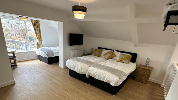 A bedroom with a large bed, a TV, a radiator, and a window with curtains. - The Highmead (Blackwood)