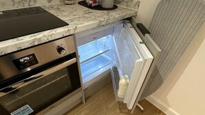 A compact kitchen with a built-in oven, a refrigerator, and a microwave. - The Highmead (Blackwood)