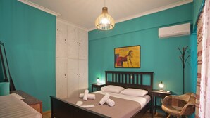 Une chambre avec des murs de couleur turquoise, un lit en bois, une table de chevet avec une lampe, une chaise et un appareil de climatisation.