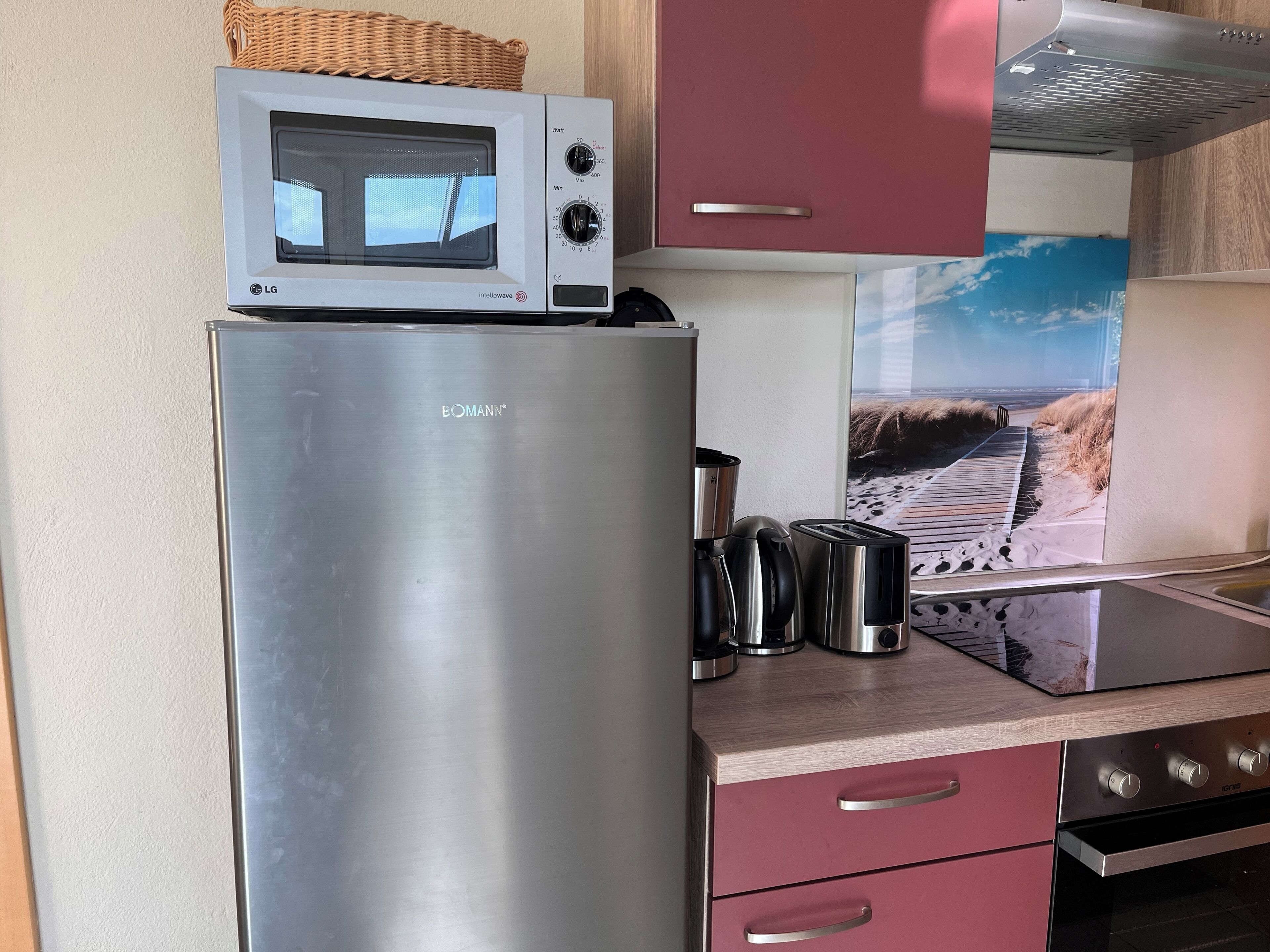 Uma cozinha com geladeira de aço inoxidável, micro-ondas, torradeira e chaleira.
