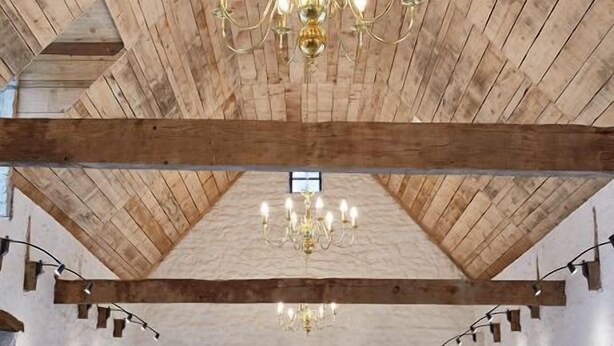 A spacious room with exposed wooden beams, a large chandelier, and a view through a sliding glass door. - Le Jardin Saint Germain Lodges & Events (Plogastel-Saint-Germain)