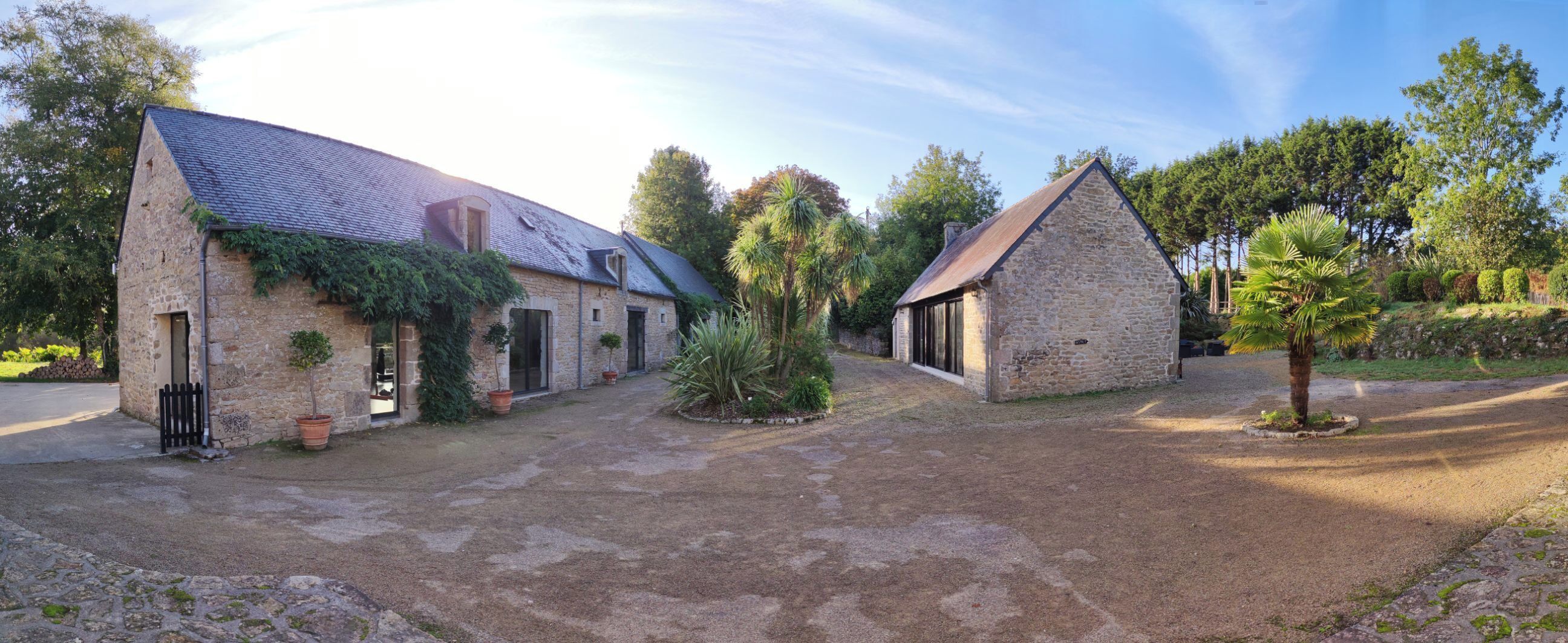 Un bâtiment en pierre avec un toit en pente, une allée pavée et de la verdure tout autour.