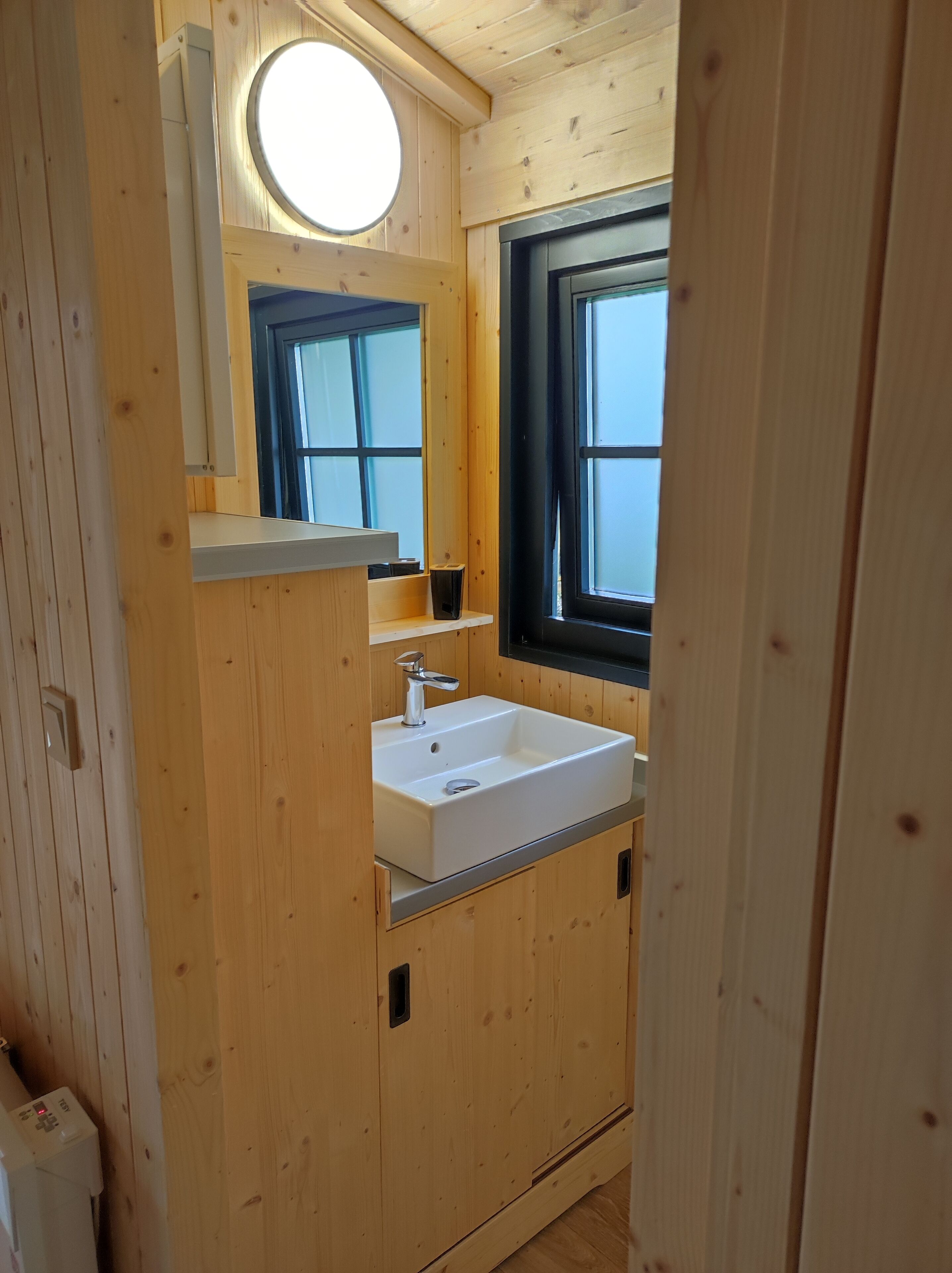 Une salle de bain en bois avec un lavabo blanc, un miroir et une fenêtre.