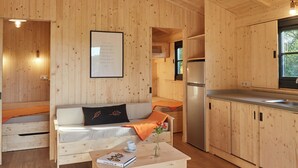 A wooden cabin interior with a sofa, a coffee table, a refrigerator, and a kitchen area. - Le Jardin Saint Germain Lodges & Events (Plogastel-Saint-Germain)
