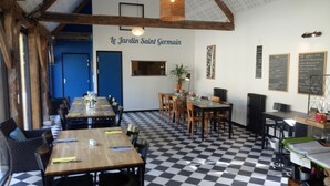 A restaurant interior with checkered flooring, wooden tables, and chairs. There is a wall with a sign reading "Le Jardin Saint Germain". - Le Jardin Saint Germain Lodges & Events (Plogastel-Saint-Germain)