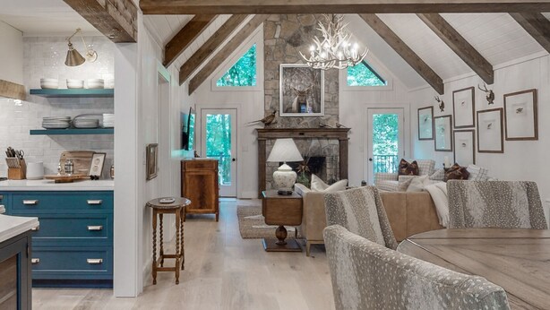 A spacious living area with a fireplace, a dining table, and a kitchen with blue cabinets. - Luxury cabin w/ chef kitchen & two living rooms (Highlands)