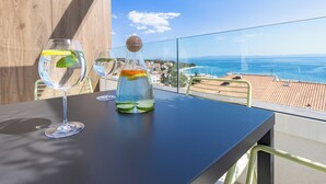 Una mesa con dos vasos de agua y una botella de jugo de naranja en un balcón con vista al mar.