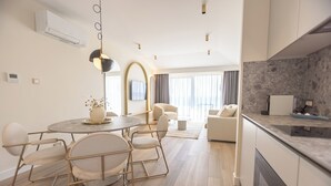 Una sala de estar moderna y bien iluminada con una mesa de comedor redonda, asientos cómodos y una cocina con encimera de mármol.