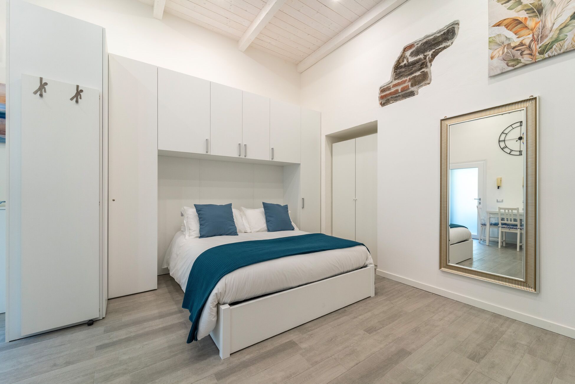 A bedroom with a bed, white wardrobe, and a large mirror.
