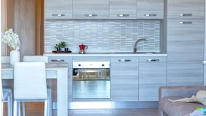 A modern kitchen with a built-in oven, a sink, and a dining area with a white table and chairs. - Sardinia Re - Smeralda 16 (Castelsardo)