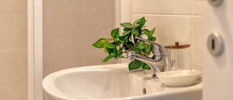 A bathroom sink with a modern faucet, a small bowl, and a potted plant.