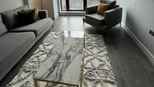 A modern living room with a grey sofa, a smaller armchair, a marble coffee table, and a large window with a city view.