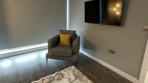 A modern living room with a grey sofa, a large window, a flat-screen TV, and a marble-patterned rug.