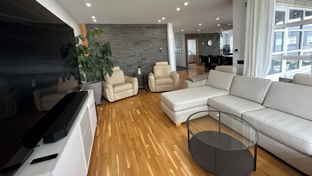 Een moderne woonkamer met een grote flatscreen televisie, leren banken, een glazen salontafel en een potplant.