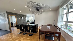 Een moderne eetruimte met een houten tafel en stoelen, een bijzondere plafondlamp en grote ramen voor natuurlijk licht.
