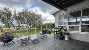 Een terras met een barbecue, lounge stoelen en uitzicht op de achtertuin.