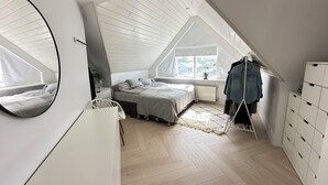 Une chambre avec un plafond en pente, un lit, une commode, un miroir et une fenêtre.