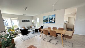 Un salon moderne avec un coin repas, comprenant une grande table en bois, des sièges en cuir et une vue sur l’extérieur.