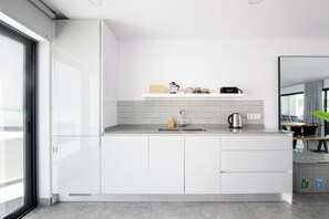 Cozinha moderna com armários brancos, pia de aço inoxidável e bancada com chaleira e potes.