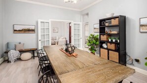 Zona pranzo con tavolo in legno, sedie, un lampadario e una libreria.
