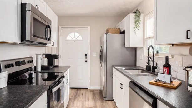 Una cocina moderna con armarios blancos, electrodomésticos de acero inoxidable y piso de madera.