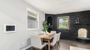 A dining area with a wooden table and chairs, a black brick fireplace, and two windows with blinds. - Suburban oasis perfect for families & groups (Columbus)