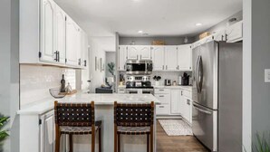 A modern kitchen with white cabinetry, stainless steel appliances, and a central island with two chairs. - Suburban oasis perfect for families & groups (Columbus)