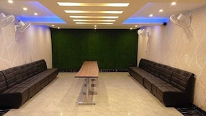 A spacious room with a green wall, two black sofas, a wooden table, and a tiled floor.