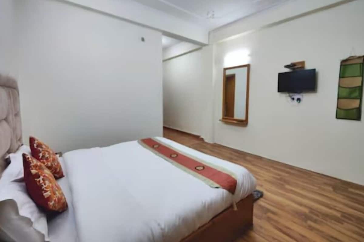 A bedroom with a bed, a wooden floor, a TV, and a mirror on the wall.