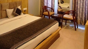 A hotel room with a bed, a desk, two chairs, a mirror, and curtains.