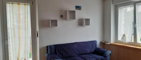 A room with a blue sofa, a door with a curtain, and three wall-mounted shelves.