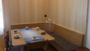 Une table de salle à manger en bois, quatre chaises, un banc le long du mur et une petite statue accrochée au mur.