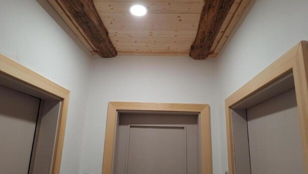 Un couloir avec des poutres en bois au plafond, un éclairage encastré et trois portes dotées de cadres en bois.