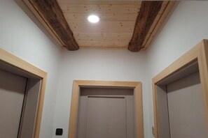 Un couloir avec des poutres en bois au plafond, un éclairage encastré et trois portes dotées de cadres en bois.