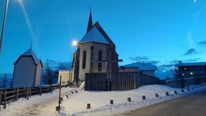 Une église dotée d’un flèche pointue et d’un clocher, entourée d’un paysage enneigé et d’une clôture en bois.