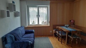 Une pièce avec un canapé bleu, une table à manger en bois avec des chaises, et une fenêtre à vitres dépolies.